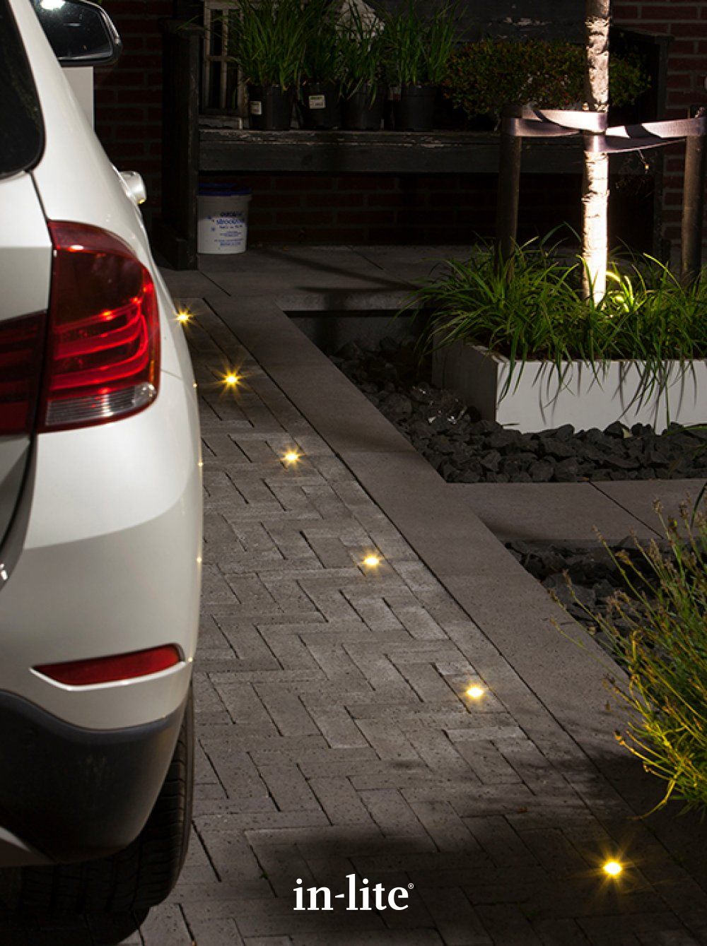 in-lite outdoor lights integrated into a paved driveway beside a landscaped planting bed at night